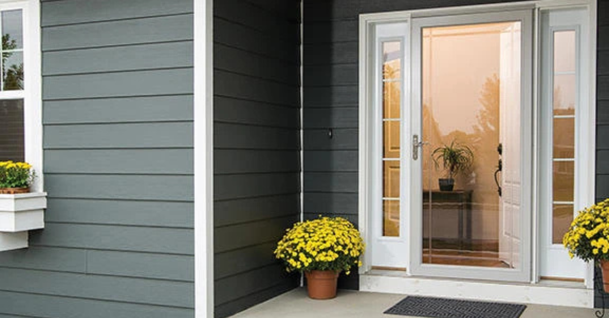 A gray house exterior with white trim, a glass front door, yellow potted flowers, and a small indoor plant visible inside the entryway—perfect for Phoenix living.