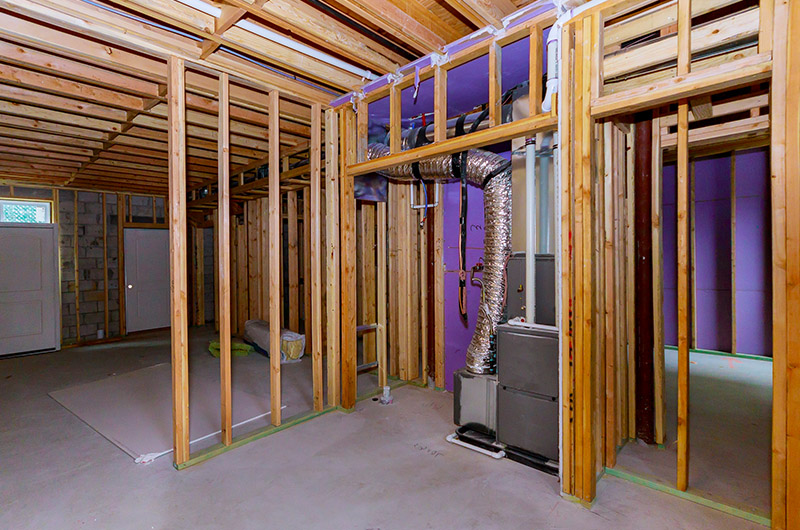 Unfinished basement with exposed wooden framing and a furnace unit, ideal for a custom basement remodeling project. Walls lack drywall, offering a blank canvas for your design vision. Transform the concrete floor into something spectacular with expert remodeling services available in Arizona.