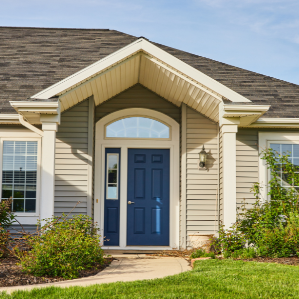 Front entrance of an Arizona house with beige siding, white trim, a blue exterior door replacement, arched window above the door, and a small porch light on the right side. Shrubs and green lawn in front.