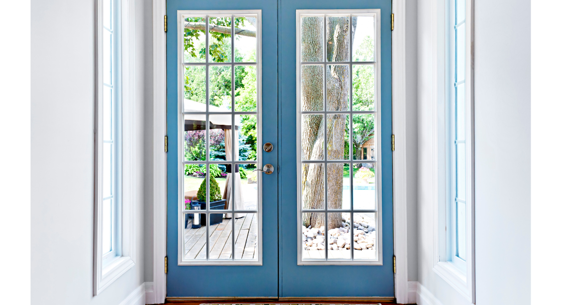 A set of blue double French doors with glass panes combines elegance with security features, offering a view of a wooden deck, outdoor furniture, and a tree in the backyard.