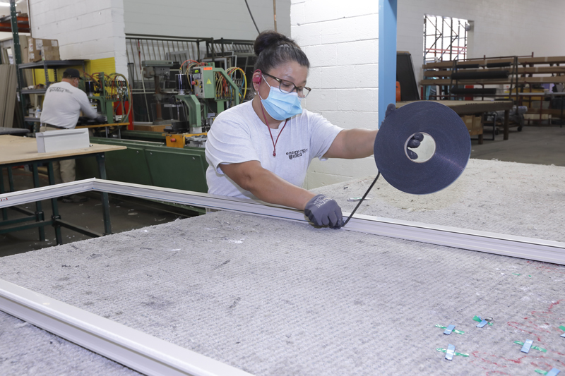 A woman wearing a face mask is working in a factory producing replacement windows.