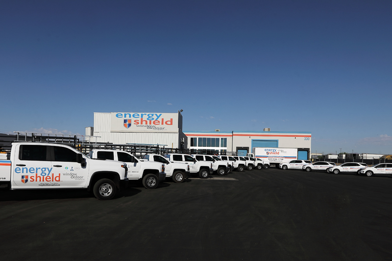 A fleet of white trucks parked in front of a building, representing a window replacement company.